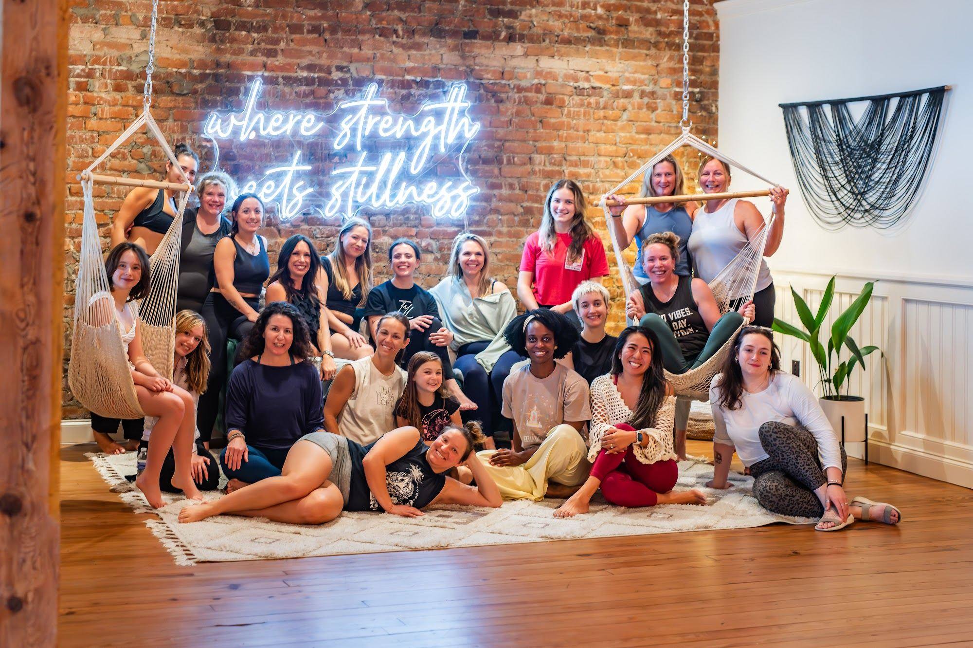 A large group of students gathered under the neon sign at The Yoga Loft